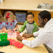 A man helps children sitting at a table.